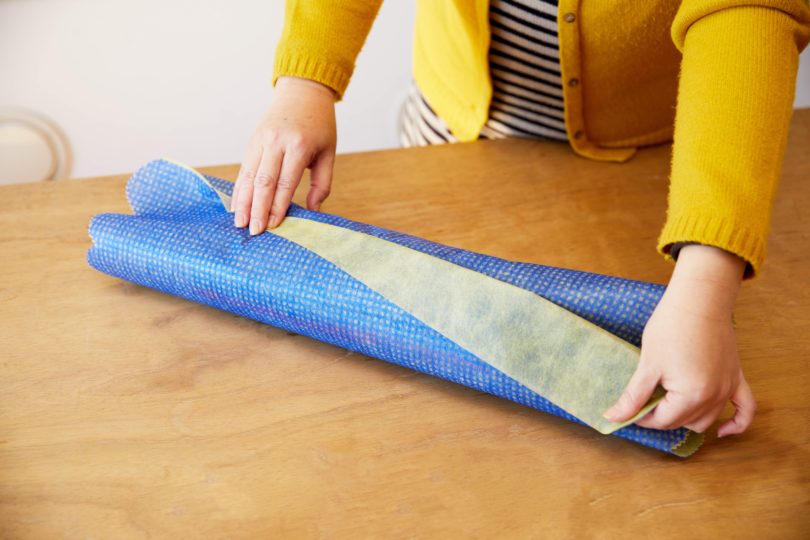 カットした辺をタテ向きに不織布を広げ、巻いたタオルをヨコ向きに置く。